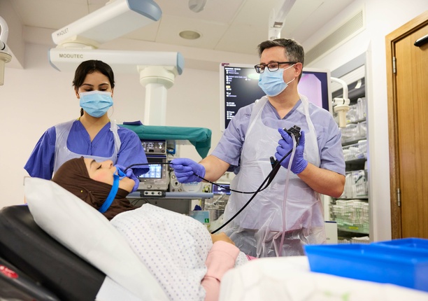 A photo of a consultant and nurse in the background, with a patient lying on a hospital bed at TLC, undergoing a diagnostic test.