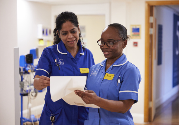 Two London Clinic nurses in blue uniform, smiling and looking at a piece of paper.