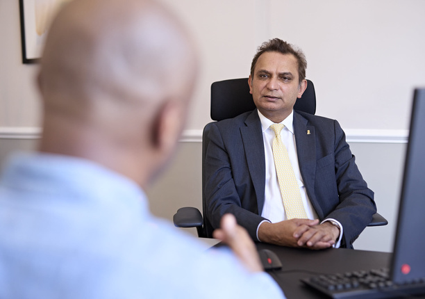 A candid photo of a consultation taking place. We see the back of a patient's head and in focus and the background is Professor Prokar Dasgupta, mid-conversation with the patient.