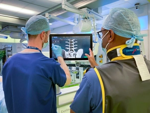Two people in scrubs stand looking at the screen of a surgical robot