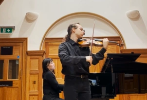 Leslie Wilburn holding a violin with a piano in the background