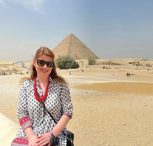 A photo of the London Clinic patient, Andrea, in the foreground with the pyramids of Egypt behind her, smiling and happy.