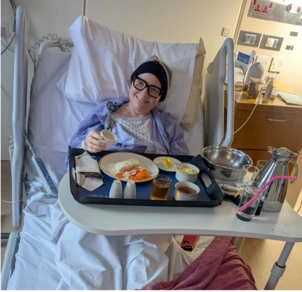 A photo of patient Andrea in a London Clinic hospital bed smiling eating breakfast!