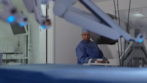 A photo of the da vinci robot in the foreground of the image, with consultant Prokar Dasgupta in the background by the unit which controls the robot.