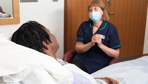 Masked nurse sits with patient