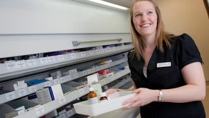 A pharmacist smiling whilst holding medication