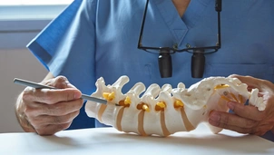 A neurosurgeon using pencil pointing at lumbar vertebra model in medical office