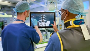 Two people in scrubs stand looking at the screen of a surgical robot