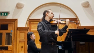 Leslie Wilburn holding a violin with a piano in the background