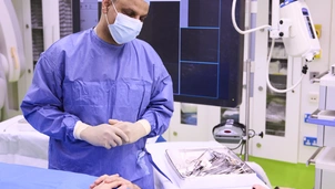 A consultant in scrubs with a patient (awake) lying on a bed. They are having a conversation