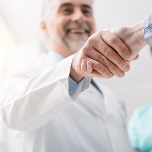 A doctor and a patient shaking hands whilst smiling