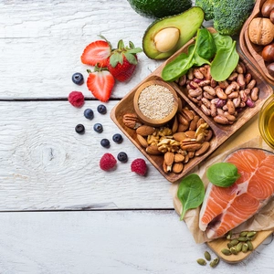 Image of food depicting healthy eating, fruits, salmon, nuts, veg, oil on textured white background