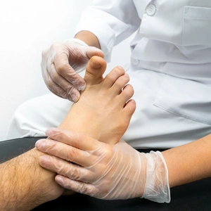 Close-up of a podiatrist performing an examination of a patient on a stretcher. The doctor is wearing gloves and moving the patient's big toe