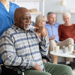 Disabled african american senior man in wheelchair holding nurse hand, looking at copy space and smiling, thanking for support, life in nursing home for elderly people concept