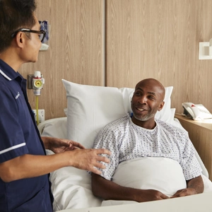 A man in a TLC hospital bed smiling at a clinical nurse specialist