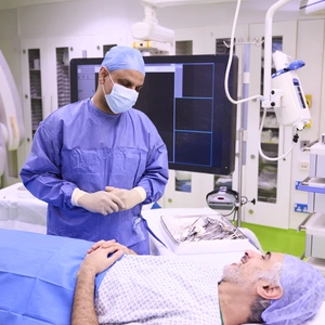 A consultant in scrubs with a patient (awake) lying on a bed. They are having a conversation