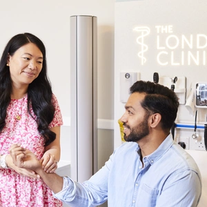 A London Clinic female, private GP, checking pulse on a male patient's wrist. Both smiling. Patient receiving a GP check-up