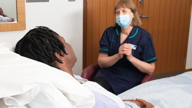 A nurse sat next to a bed talking to a patient